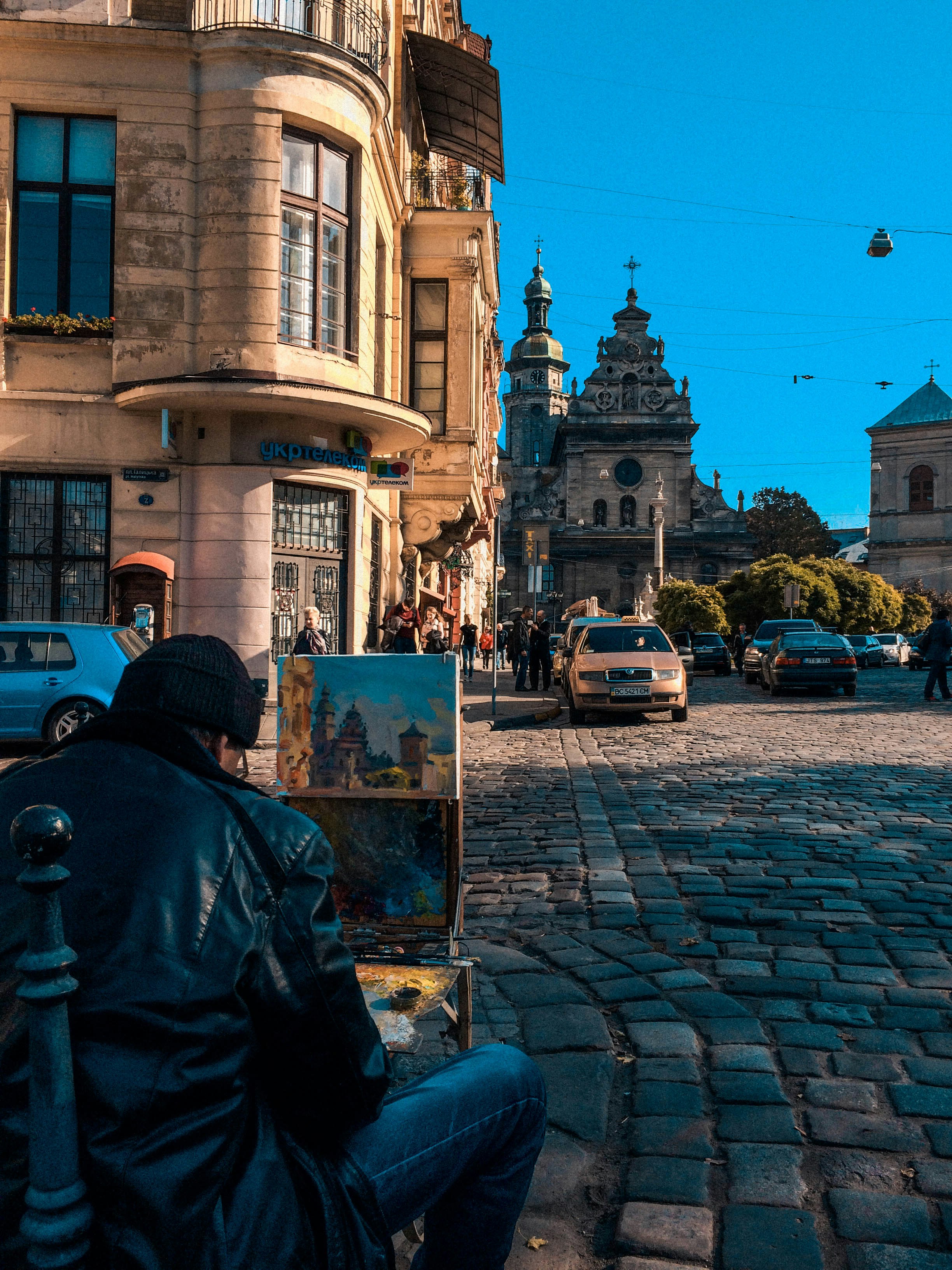 man in black jacket standing near cars and buildings during daytime