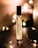 A perfume bottle labeled 'Nutmeg 26 MORRA Autumn No.2 eau de parfum' stands upright on a dark surface. Soft, warm lighting surrounds the bottle, creating a cozy and intimate atmosphere. Small, fairy lights are elegantly arranged around the bottle, adding a touch of sparkle and enhancing the ambient glow.