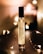 A perfume bottle labeled 'Nutmeg 26 MORRA Autumn No.2 eau de parfum' stands upright on a dark surface. Soft, warm lighting surrounds the bottle, creating a cozy and intimate atmosphere. Small, fairy lights are elegantly arranged around the bottle, adding a touch of sparkle and enhancing the ambient glow.