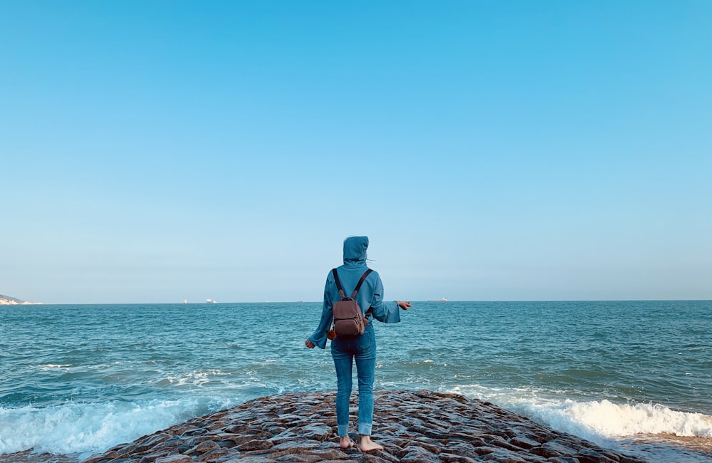 man in blue jacket standing on rocky shore during daytime