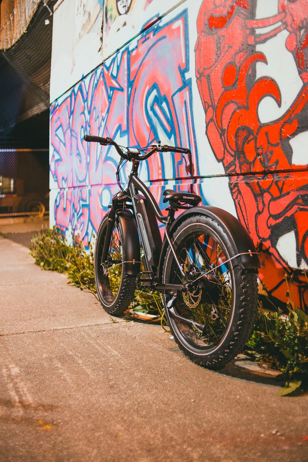 black and orange mountain bike parked beside wall with graffiti