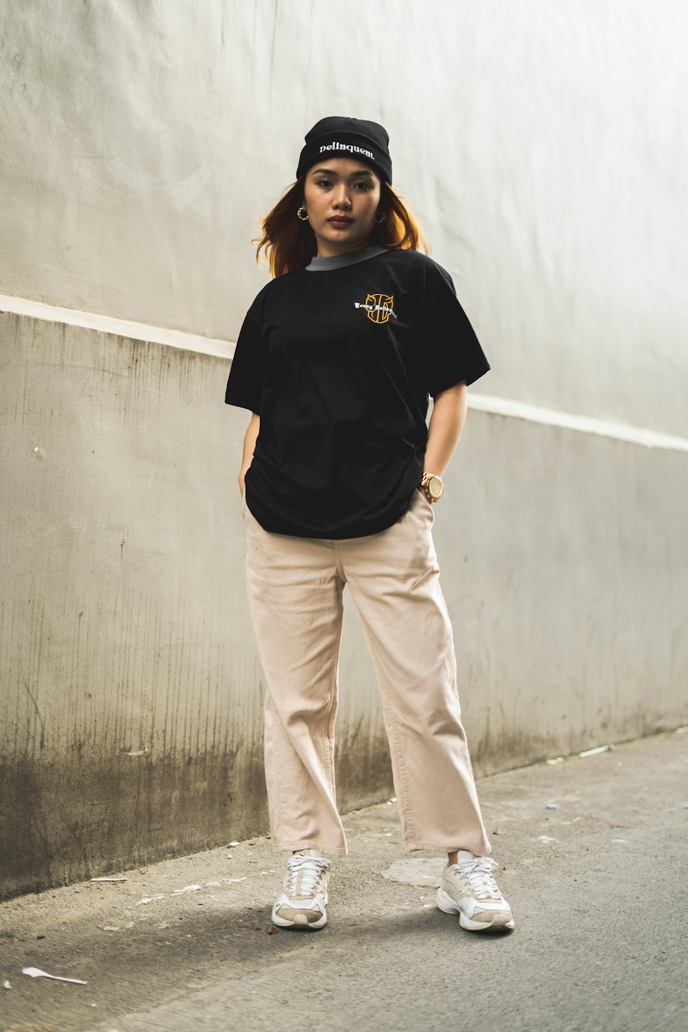 woman in black crew neck t-shirt and white pants standing beside gray wall