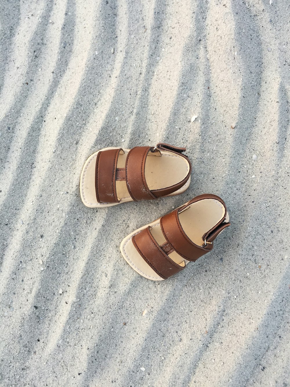 brown and black slide sandals on gray sand