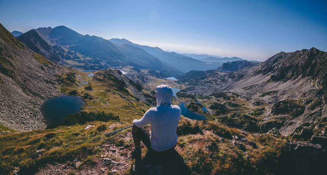 man in white shirt and black pants sitting on rock looking at mountains during daytime