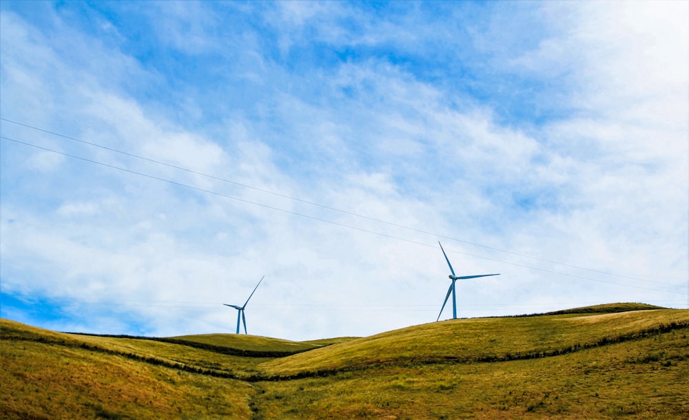 white wind turbines on green grass field under blue and white cloudy sky during daytime