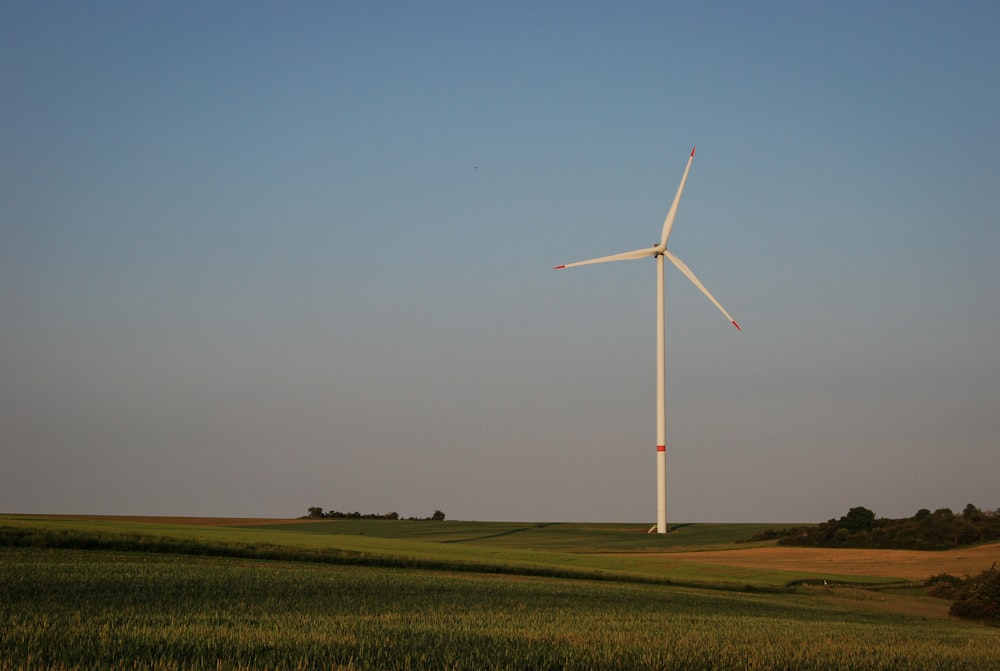 white wind turbine on green grass field under blue sky during daytime