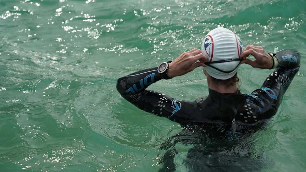 man in black wet suit wearing white and blue goggles in water