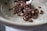 A ceramic bowl contains a small portion of chocolate-covered puffed cereal. The cereal pieces are irregularly shaped, with a glossy coating and white flecks. A metal spoon is partially visible, resting in the bowl, suggesting readiness for eating.