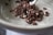 A ceramic bowl contains a small portion of chocolate-covered puffed cereal. The cereal pieces are irregularly shaped, with a glossy coating and white flecks. A metal spoon is partially visible, resting in the bowl, suggesting readiness for eating.