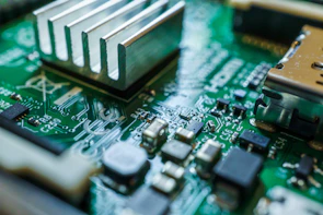 A close-up view of a green circuit board featuring various electronic components such as capacitors, resistors, and a heat sink. The intricate design of the circuitry can be seen with silver solder traces and black components set against the green base material.