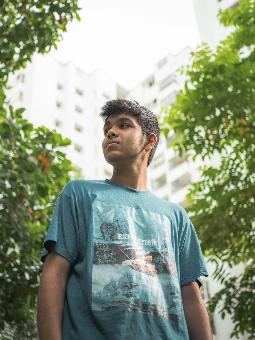 man in blue crew neck t-shirt standing near green trees during daytime