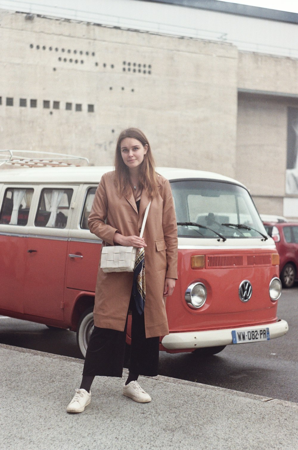woman in brown coat standing beside red and white volkswagen t-1