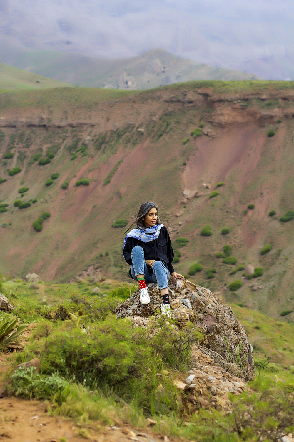 woman in blue jacket sitting on rock during daytime