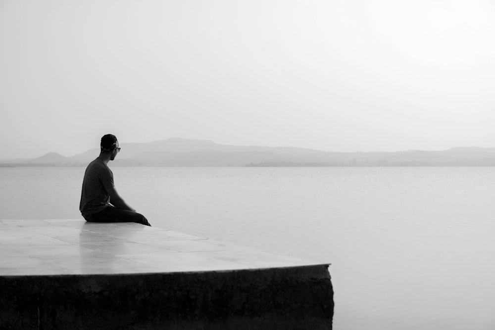 man sitting on concrete bench near body of water