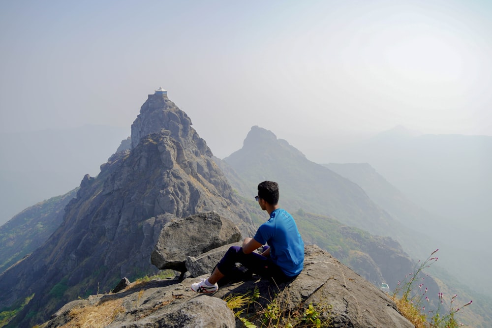 man in blue shirt sitting on rock mountain during daytime