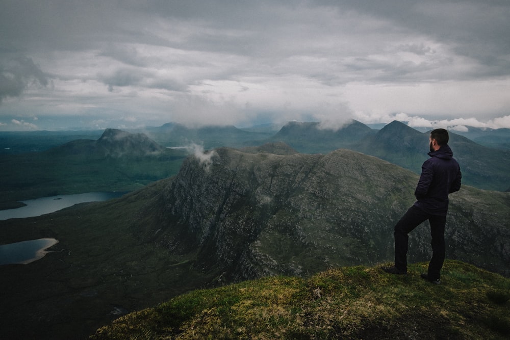 person standing on green grass field near mountain under white clouds during daytime