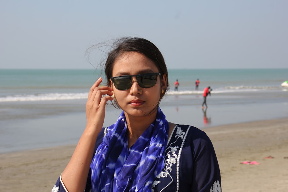 woman in black and blue floral scarf and black sunglasses standing on beach during daytime