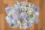 A collection of various banknotes spread out on a wooden surface, including currencies such as U.S. dollars, Euros, and Turkish lira.