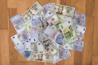 A collection of various banknotes spread out on a wooden surface, including currencies such as U.S. dollars, Euros, and Turkish lira.