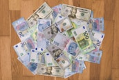 A collection of various banknotes spread out on a wooden surface, including currencies such as U.S. dollars, Euros, and Turkish lira.