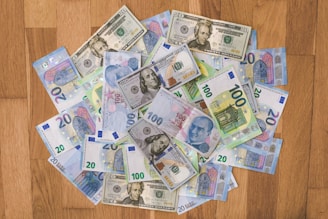 A collection of various banknotes spread out on a wooden surface, including currencies such as U.S. dollars, Euros, and Turkish lira.