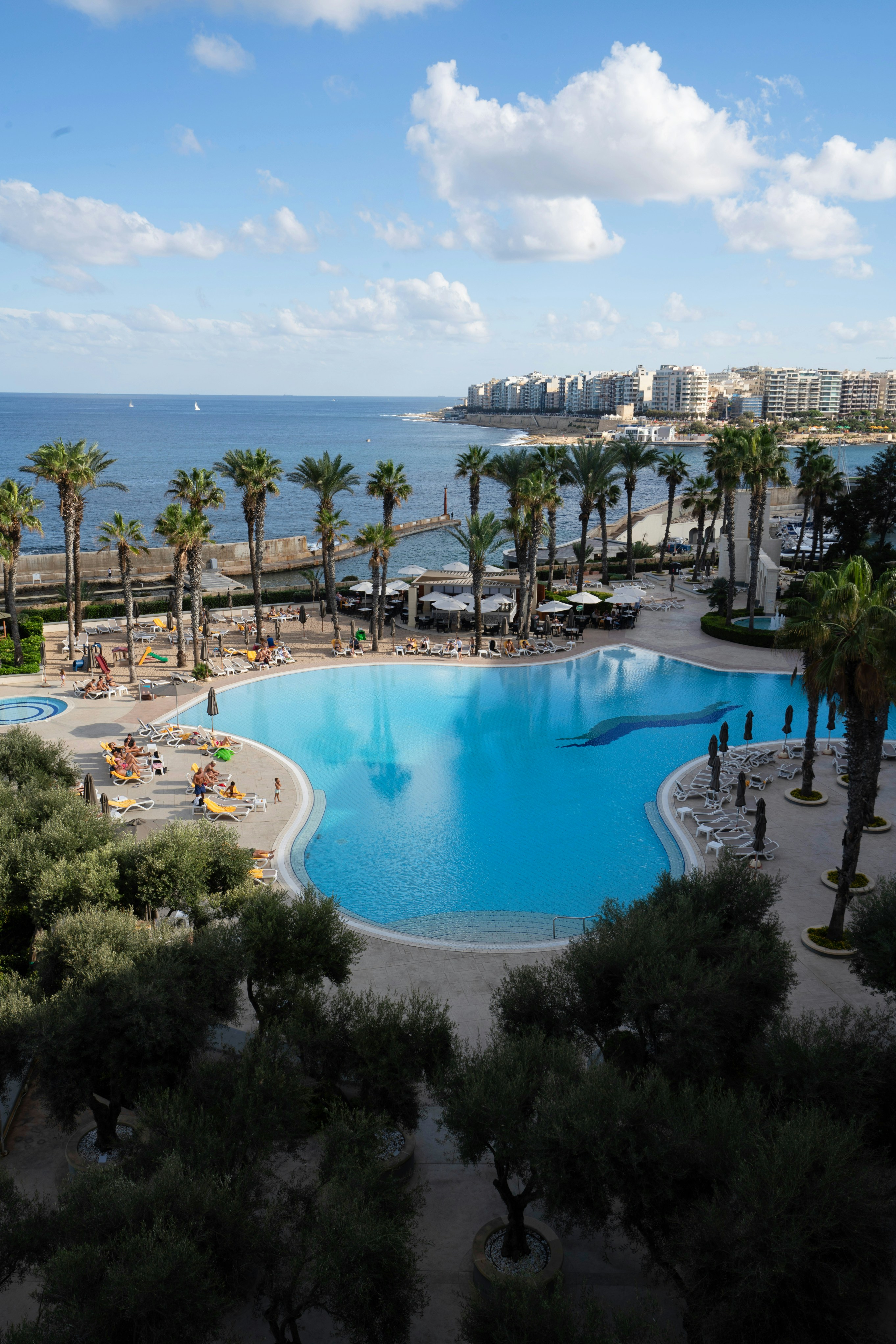 Swimming pool area of villa, outdoor terrace, blue water, sun loungers, palm trees