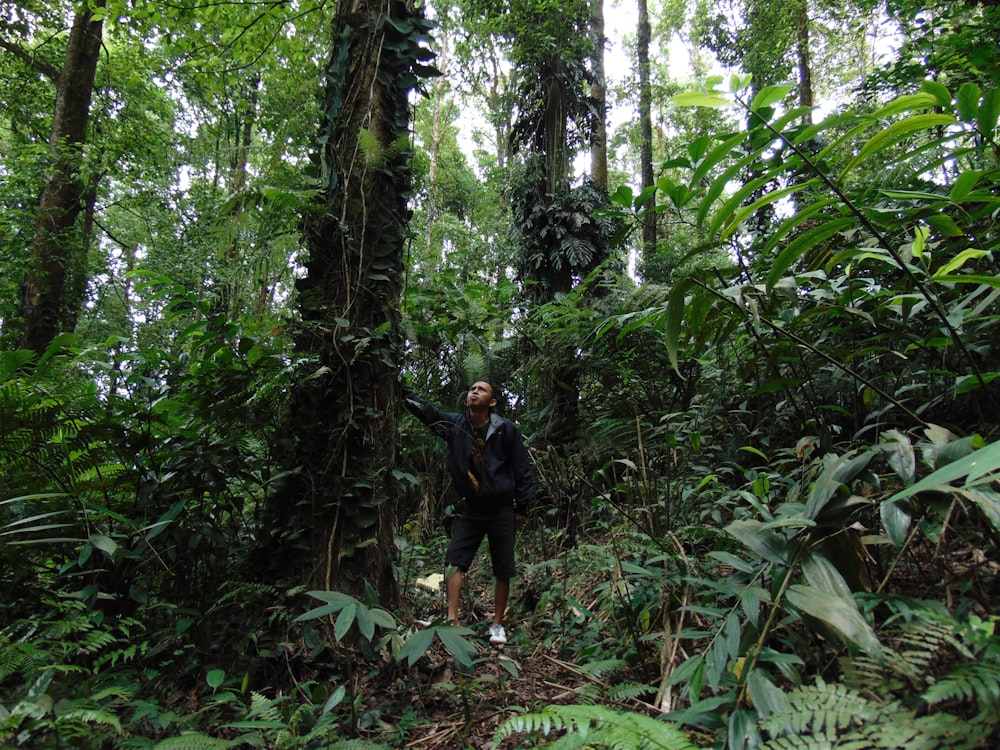 man in black shirt and black shorts standing on forest during daytime