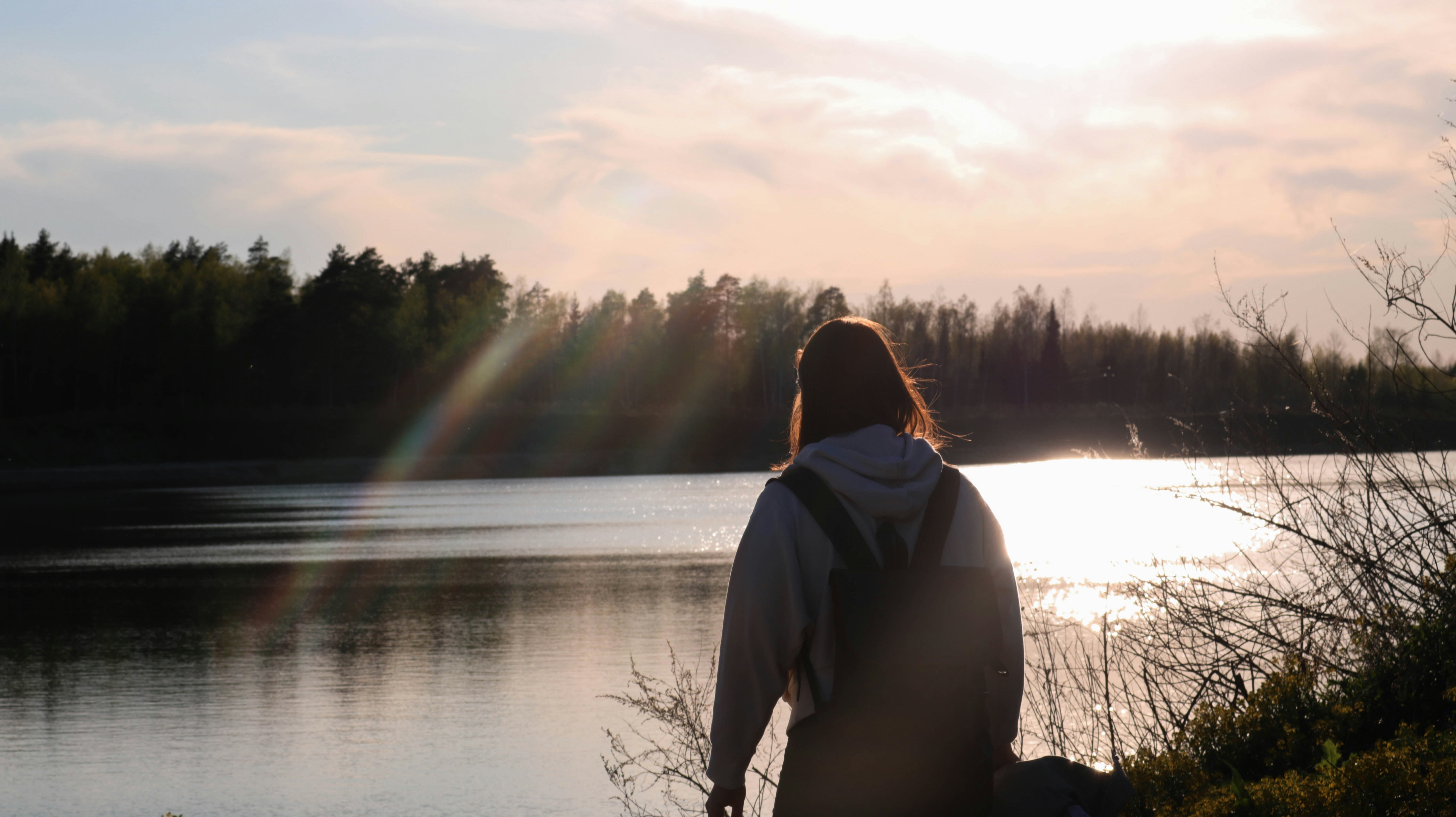 person in gray hoodie standing near lake during daytime