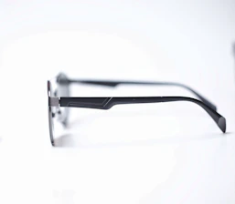 Close-up of sleek, minimalist black optical frames resting on a white surface with subtle orange accents.