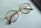 A pair of round eyeglasses with brown frames and gold temples is lying on a light blue surface. The glasses' lenses are clear, and a portion of a black object, possibly a mobile phone or case, is visible on the right edge of the image.