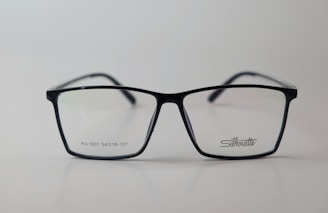 A pair of rectangular eyeglasses with a thin black frame, featuring the brand name 'Silhouette' on the right lens. The lenses are transparent, and small text is present on the left lens.