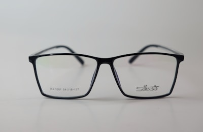 A pair of rectangular eyeglasses with a thin black frame, featuring the brand name 'Silhouette' on the right lens. The lenses are transparent, and small text is present on the left lens.