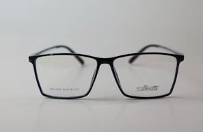 A pair of rectangular eyeglasses with a thin black frame, featuring the brand name 'Silhouette' on the right lens. The lenses are transparent, and small text is present on the left lens.