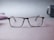 A pair of Ray-Ban eyeglasses with a sleek, rectangular frame is centered on a soft-focus surface. The muted background features hints of blurred shapes and colors, conveying a minimalist and subtle aesthetic.