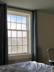 A sunlit bedroom with rich, flowing drapes framing a large window.
