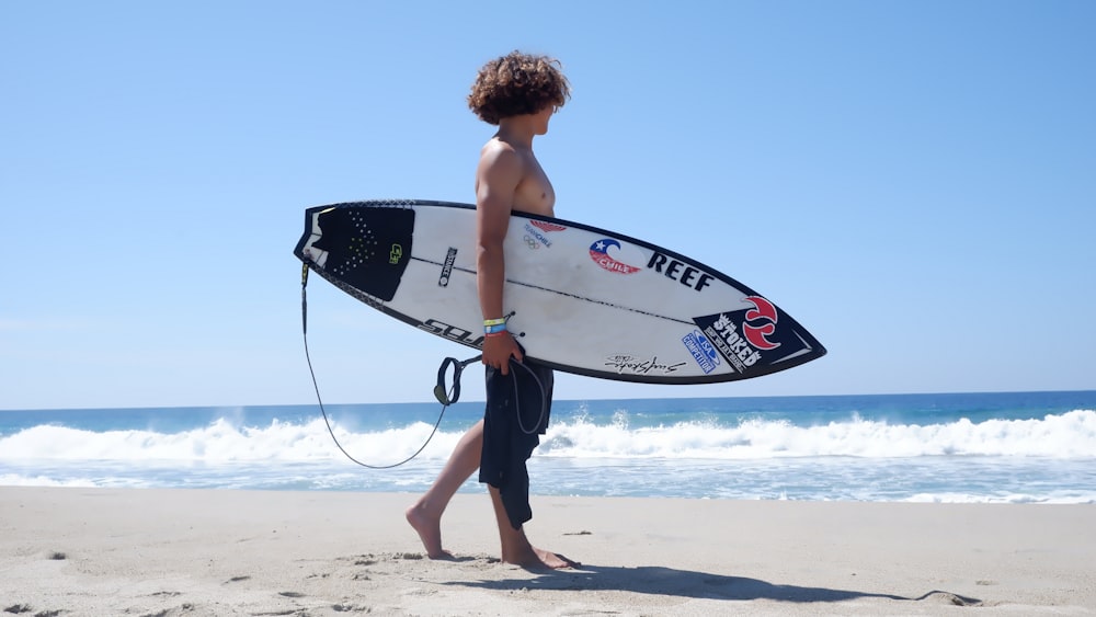 man in black shorts holding white and blue surfboard standing on beach during daytime