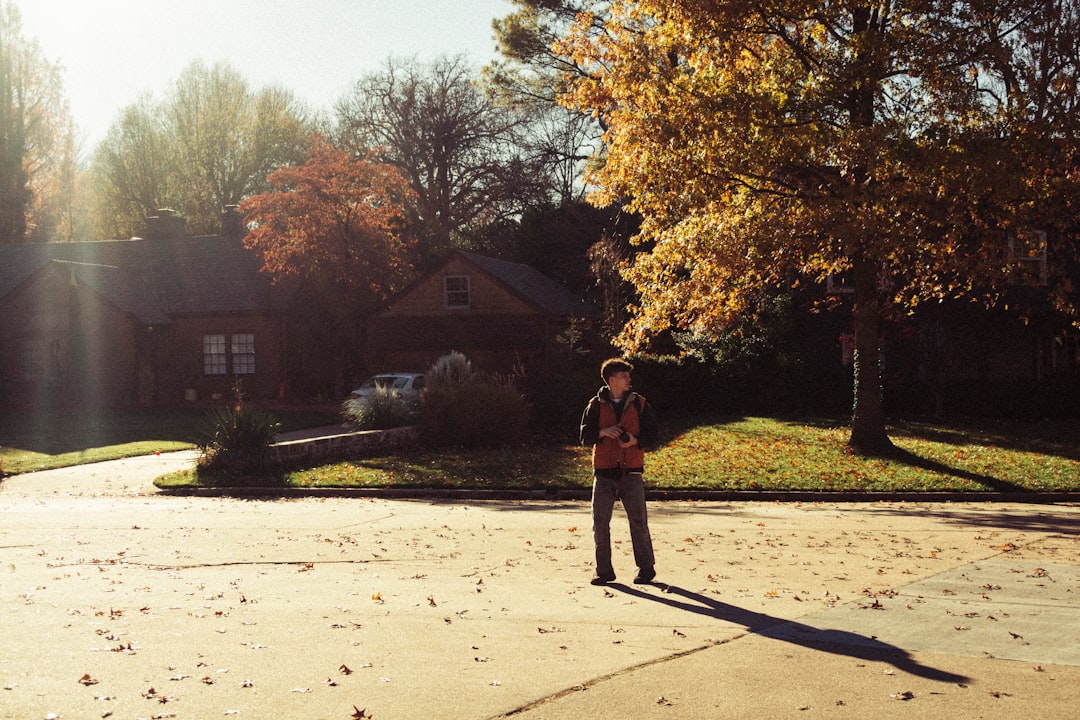 woman in red jacket standing on gray concrete pavement near brown trees during daytime