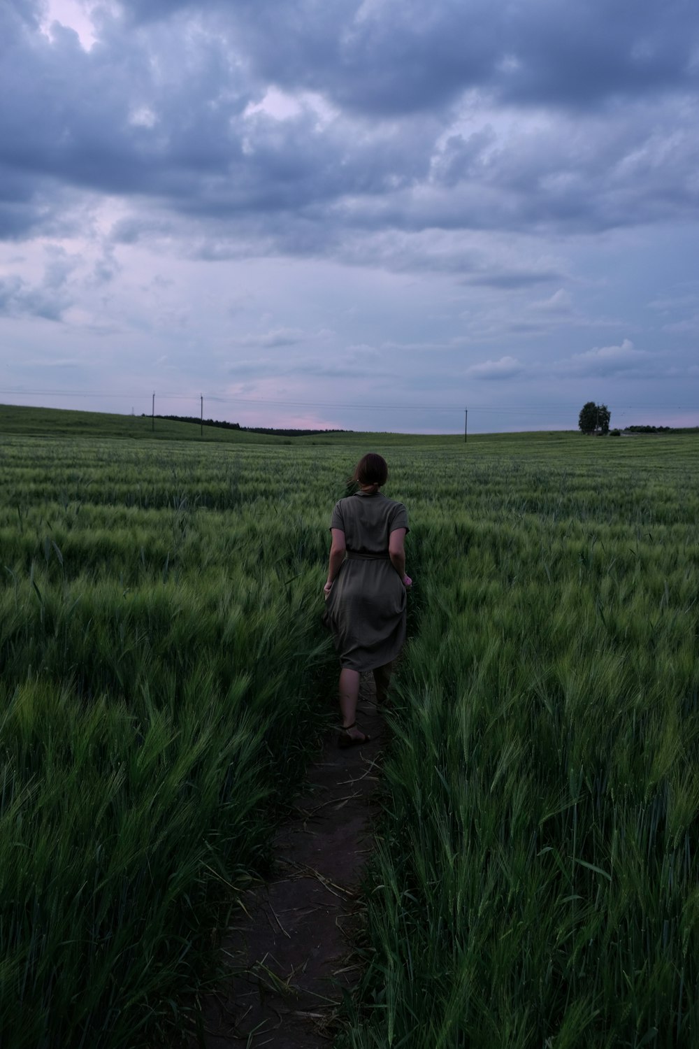 woman in gray jacket walking on green grass field during daytime