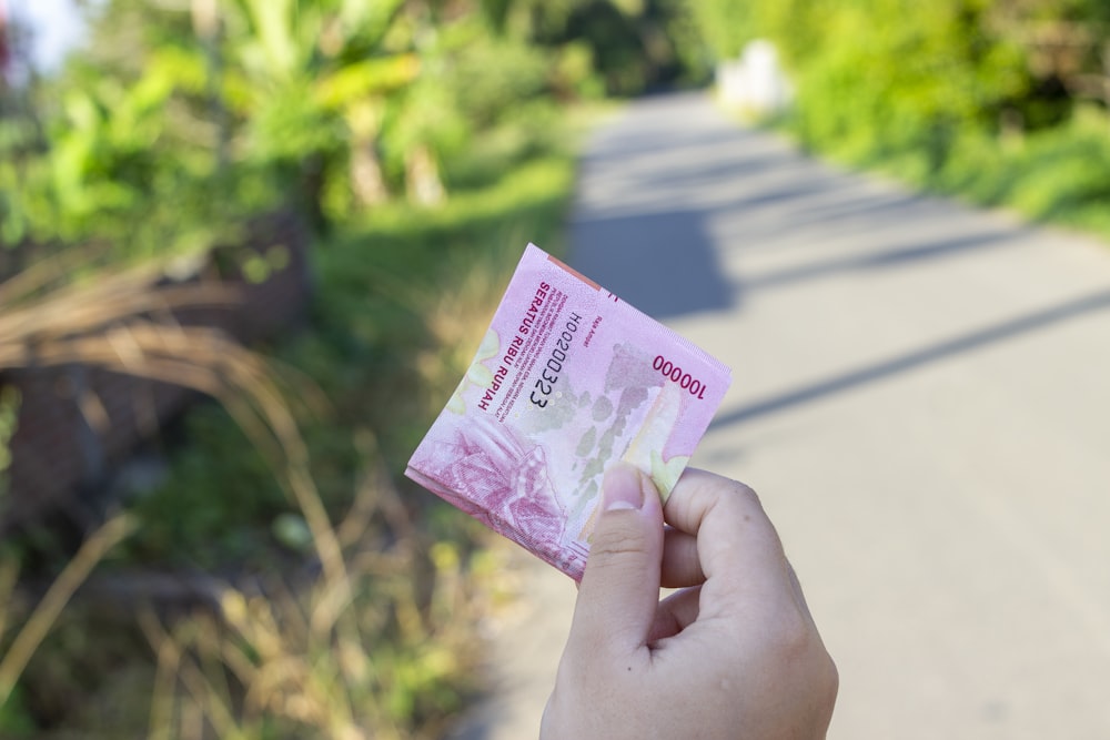 personne tenant un billet de banque rose et blanc