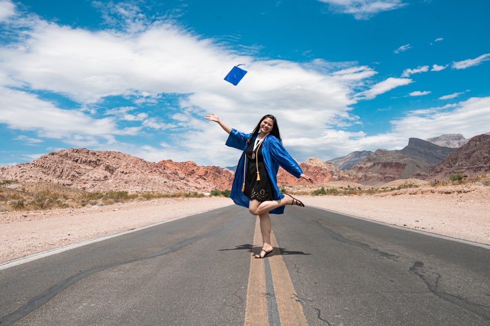mulher no vestido azul da manga comprida segurando o saco de papel azul em pé na estrada cinza do asfalto durante
