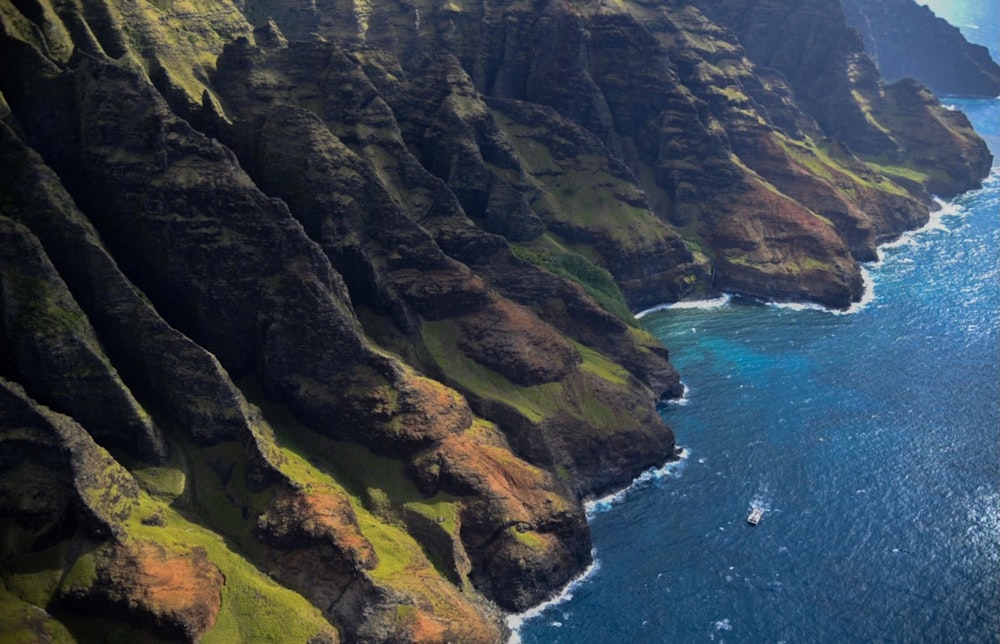 green and brown mountain beside blue sea during daytime