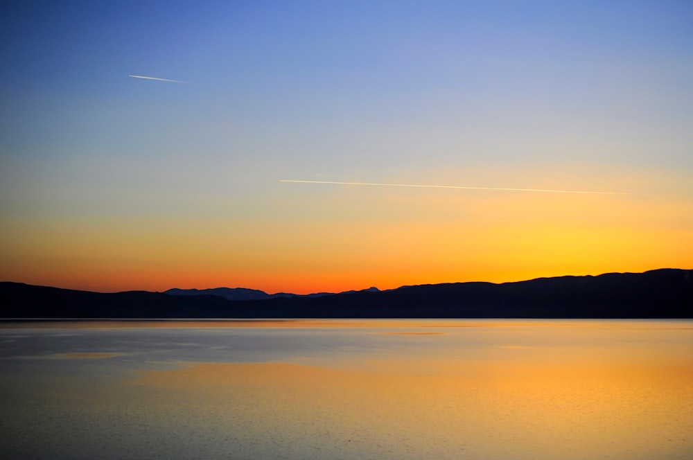 silhouette of mountain near body of water during sunset