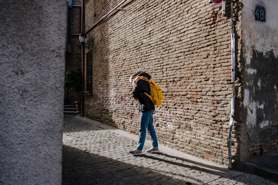 woman in yellow jacket and blue denim jeans walking on sidewalk during daytime