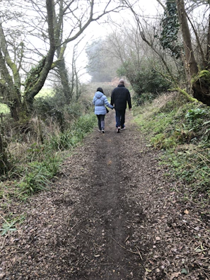 Ana and Roger walking hand in hand along a quiet path lined with trees.