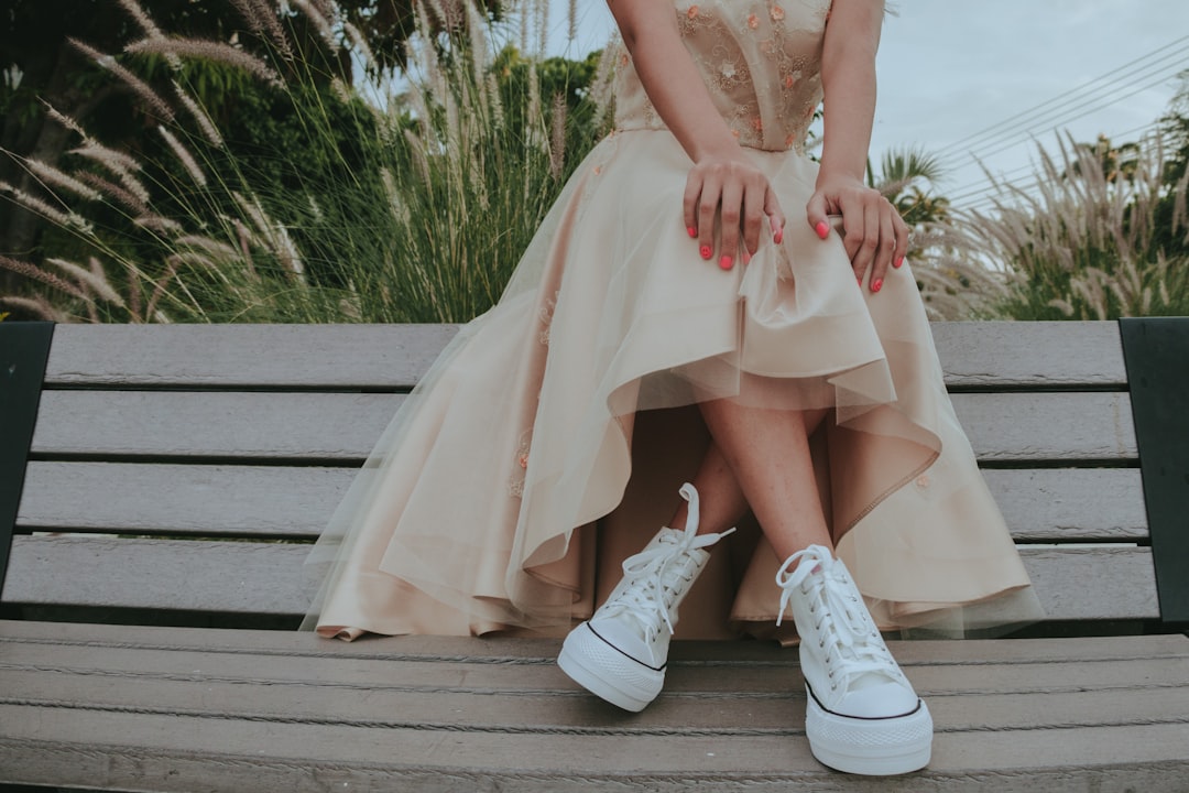 woman in white floral lace dress and white leather boots sitting on brown wooden bench