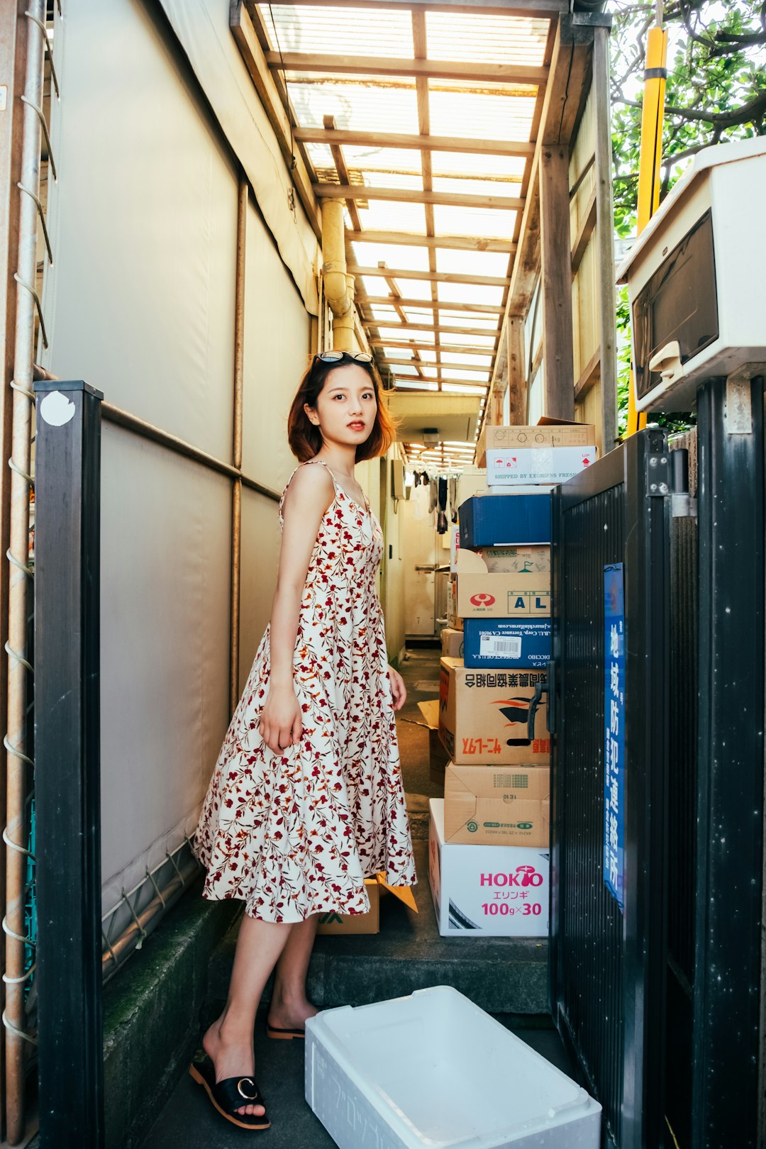 woman in black and white floral dress standing beside brown cardboard boxes