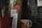 A collection of books stands against a chalkboard with various chalk drawings. A red plant pot with a wooden label marked 'Rucos' and a ceramic mug decorated with colorful flowers are positioned nearby. One of the visible books is by Gabriel Garcia Marquez.