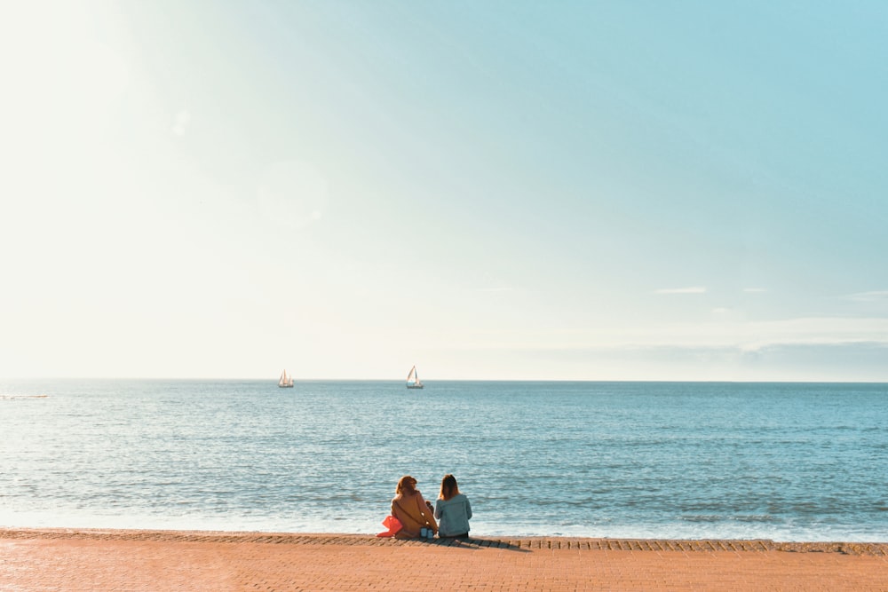 man and woman sitting on brown sand near body of water during daytime