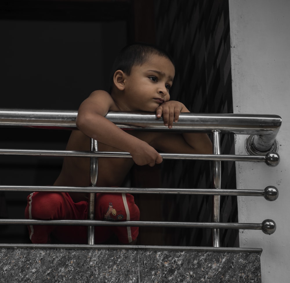 baby in red pants on stainless steel railings