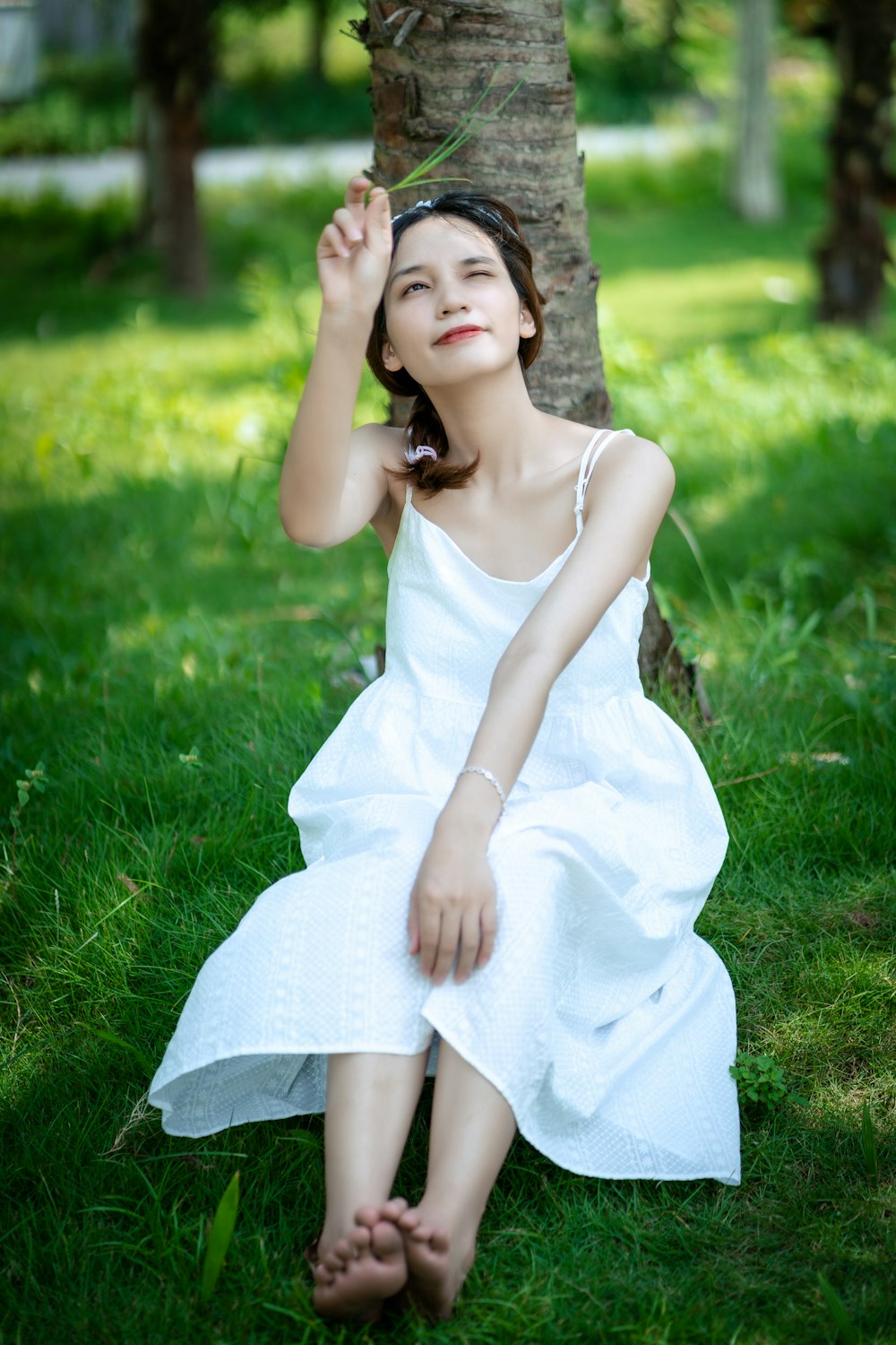 woman in white sleeveless dress sitting on green grass field during daytime